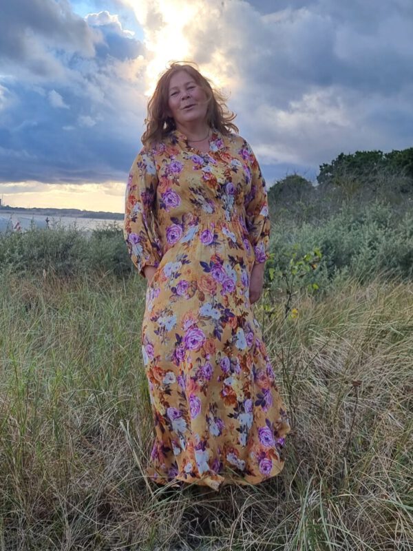 Frau in Düne stehend in einem gelben Herbstkleid mit Blumenprint in orange,lila und braun Hand in Tasche