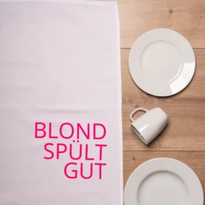 Ein weisses Geschirrtuch auf einem Tisch liegend mit dem Aufdruck in neonpink Blond spült gut