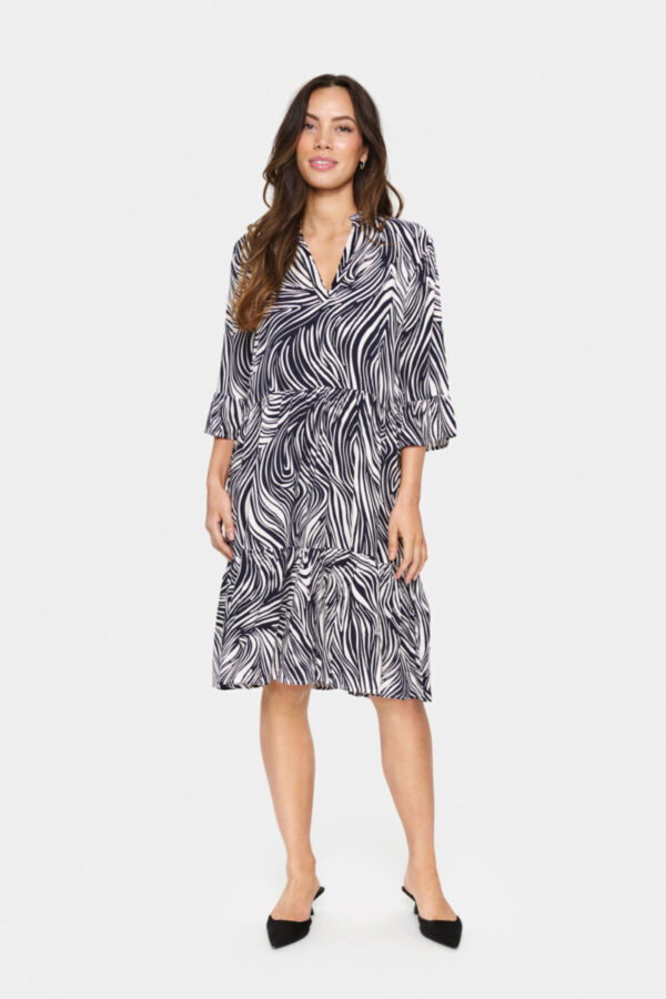Kurzes Kleid mit abstraktem Print in Off-White und Marineblau, locker geschnitten. Mit V-Ausschnitt, ellbogenlangen Ärmeln und leicht ausgestelltem Saum. Aus weichem Webstoff gefertigt. Das Model ist 175 cm groß und trägt Größe S.
