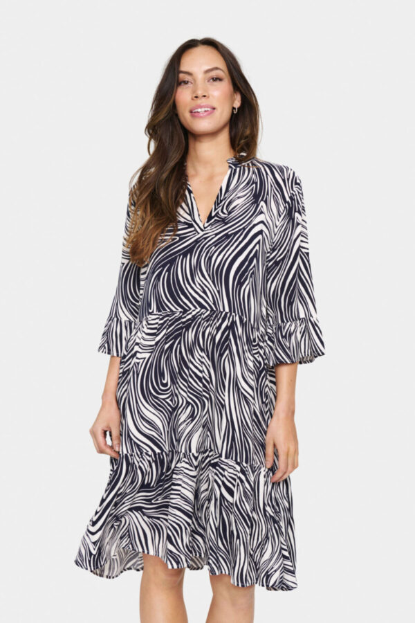 Kurzes EdaSZ Sommerkleid mit abstraktem Print in Off-White und Marineblau, locker geschnitten. Mit V-Ausschnitt, ellbogenlangen Ärmeln und leicht ausgestelltem Saum. Aus weichem Webstoff gefertigt. Das Model ist 175 cm groß und trägt Größe S.
